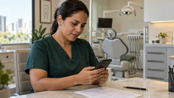 Dentista consulta o celular com um documento sobre a mesa do consultório.